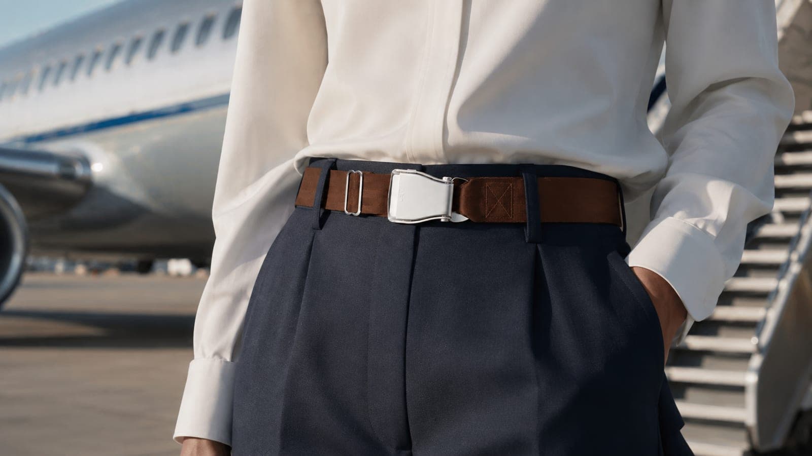 Uniforme de tripulación en la plataforma, cinturón de aviación Fly-Belts marrón en la cintura, avión y escalerilla al fondo