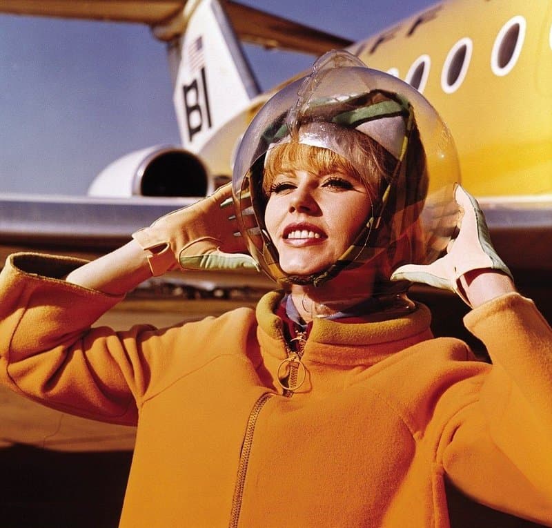 Azafata de Braniff con un conjunto naranja de Pucci y la capucha burbuja Rain Dome en plataforma