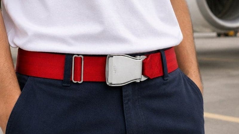 Ceinture d'avion AUSTRAL rouge profond portée avec un pantalon bleu marine devant un réacteur d'avion