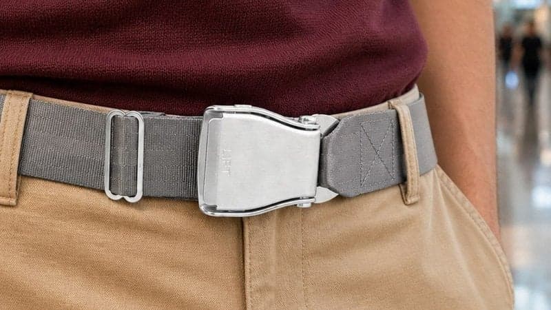 Ceinture d'avion RUNWAY grise portée avec un chino beige et un haut bordeaux dans un terminal d'aéroport