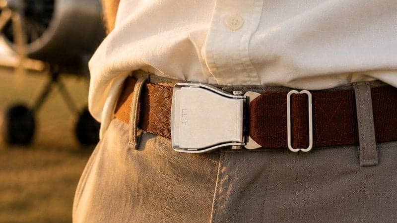 Ceinture d'avion SILK ROAD marron chaud portée avec une chemise crème, un avion à hélice ancien derrière au coucher du soleil