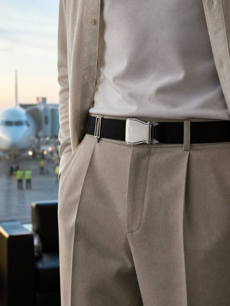 Ceinture d'avion POLAR noire portée avec un pantalon à pinces beige et une surchemise claire, dans un salon d'aéroport