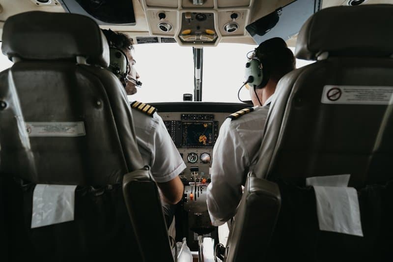 Zwei Linienpiloten in Uniform von hinten im Cockpit, die Streifen auf den Schultern sichtbar