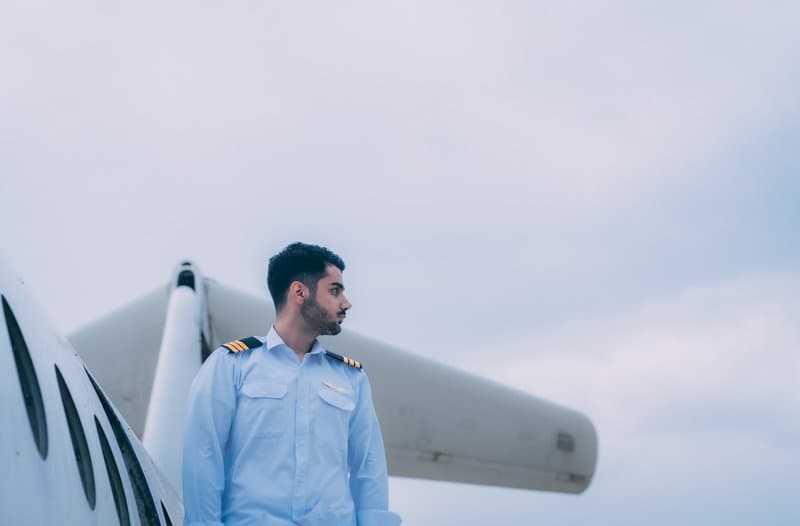 Ein junger Linienpilot in Uniform mit drei Schulterstreifen neben einem Flugzeug