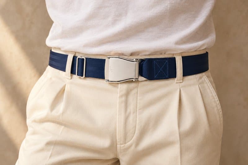 Tiefmarineblauer TRANSATLANTIC-Flugzeug-Gürtel an elfenbeinfarbener Bundfaltenhose mit weißem T-Shirt